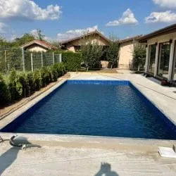 Rechteckiger Einbaupool mit weißem Beckenrand und blauem Liner in einem Hof neben einem Haus