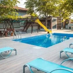Familienpool mit Holzdeck, blauen Sonnenliegen und Kinderrutsche