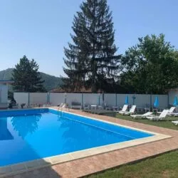 Großer Außenpool mit weißen Sonnenliegen, Sonnenschirm und Zaun im Hof